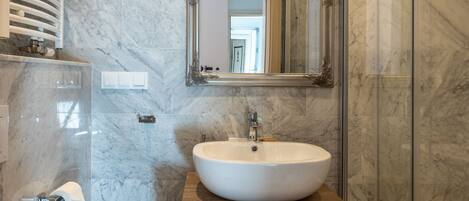 Un baño moderno con un lavabo de mármol, inodoro, cabina de ducha de vidrio y espejo sobre el lavabo.