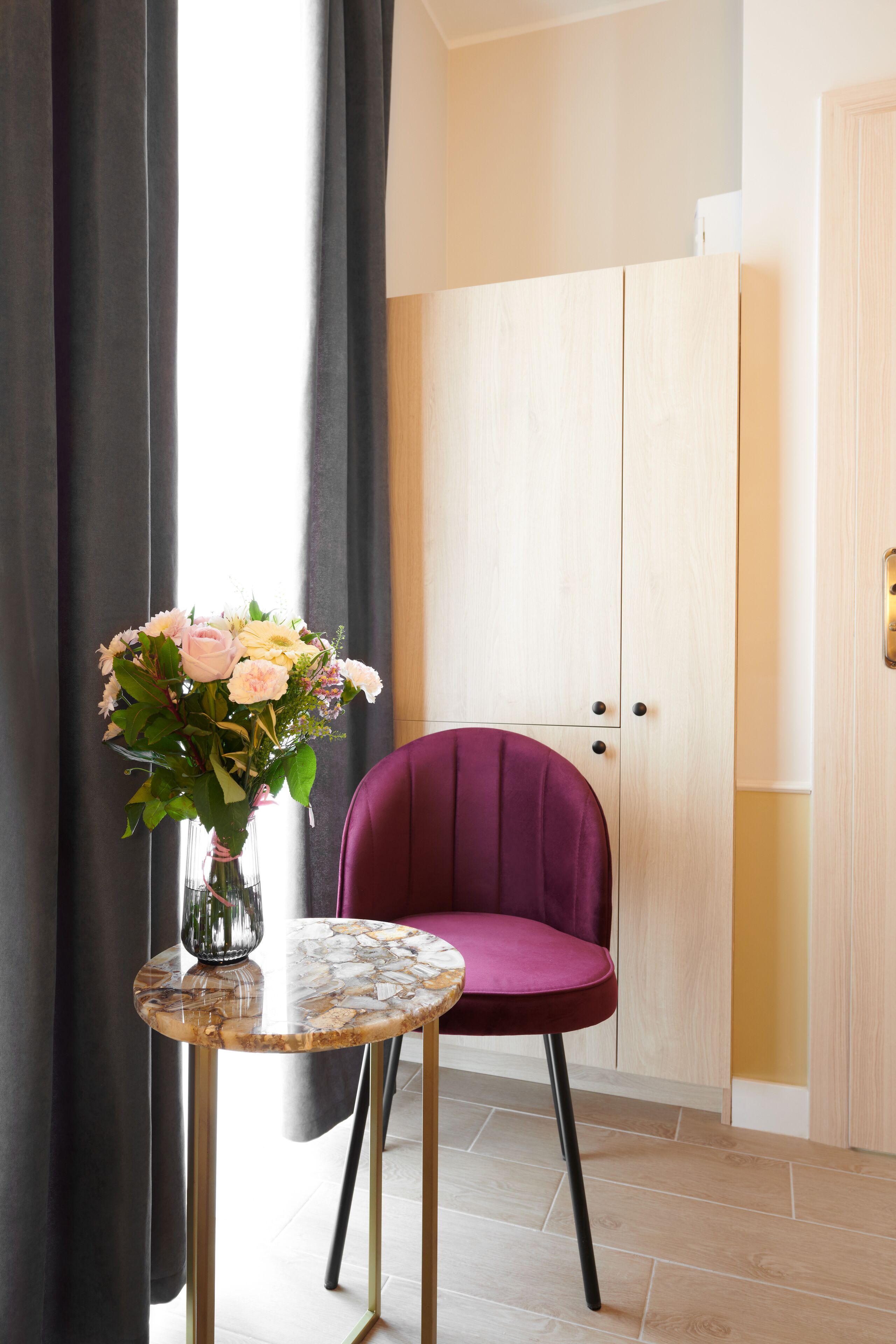 Une pièce avec une armoire en bois, une petite table ronde ornée d’un vase de fleurs et une chaise violette.