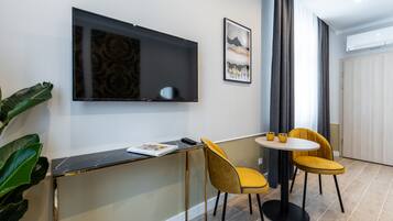 A modern room with a flat-screen TV mounted on the wall, a small round table with two yellow chairs, and a large potted plant.