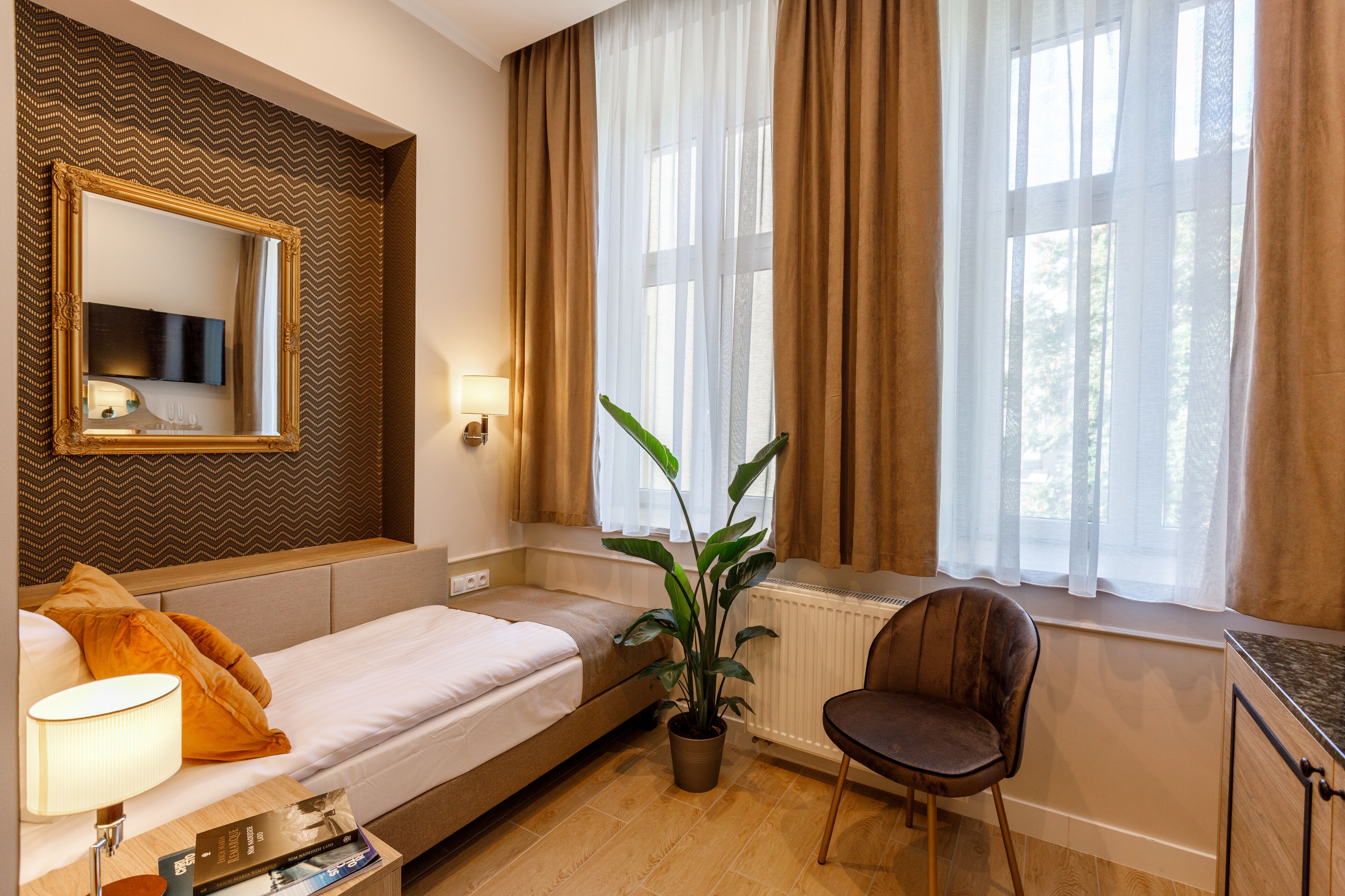 Een hotelkamer met een bed, een stoel, een bloempot, een spiegel en een raam met gordijnen.
