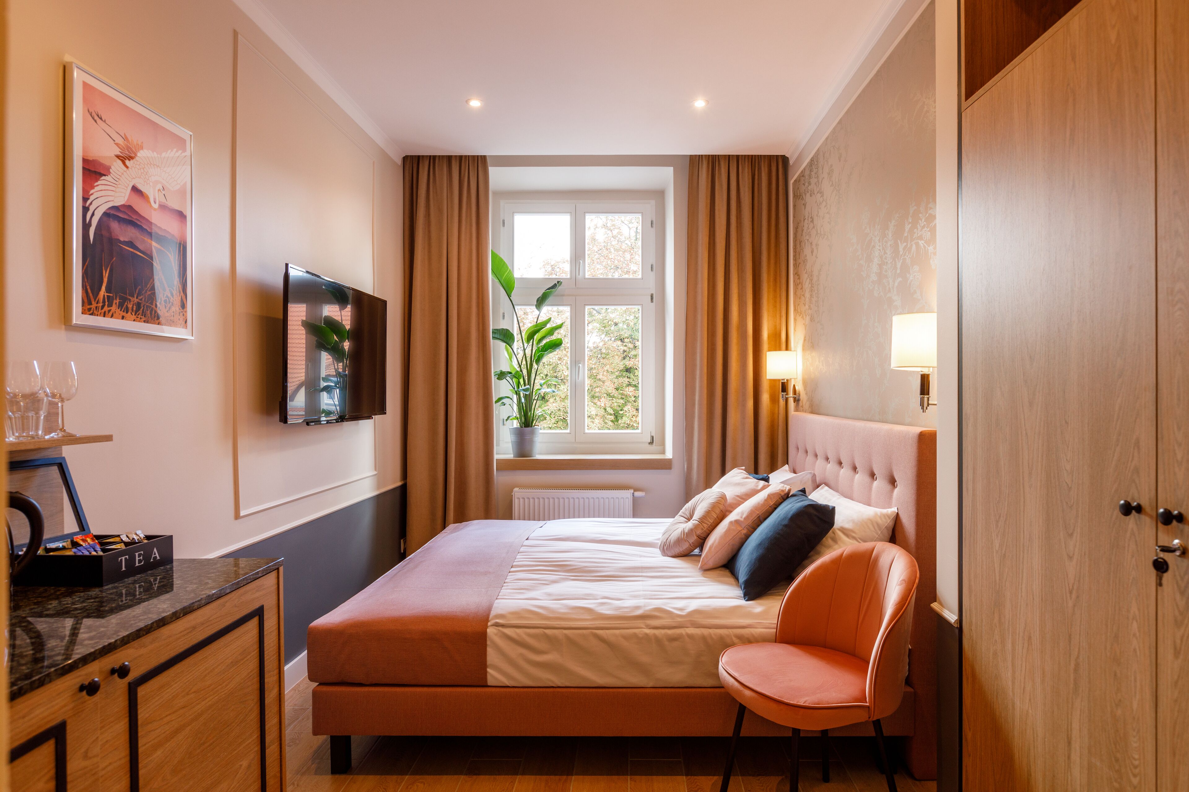 Habitación de hotel con cama, televisor, escritorio con planta, una silla y ventana con cortinas.