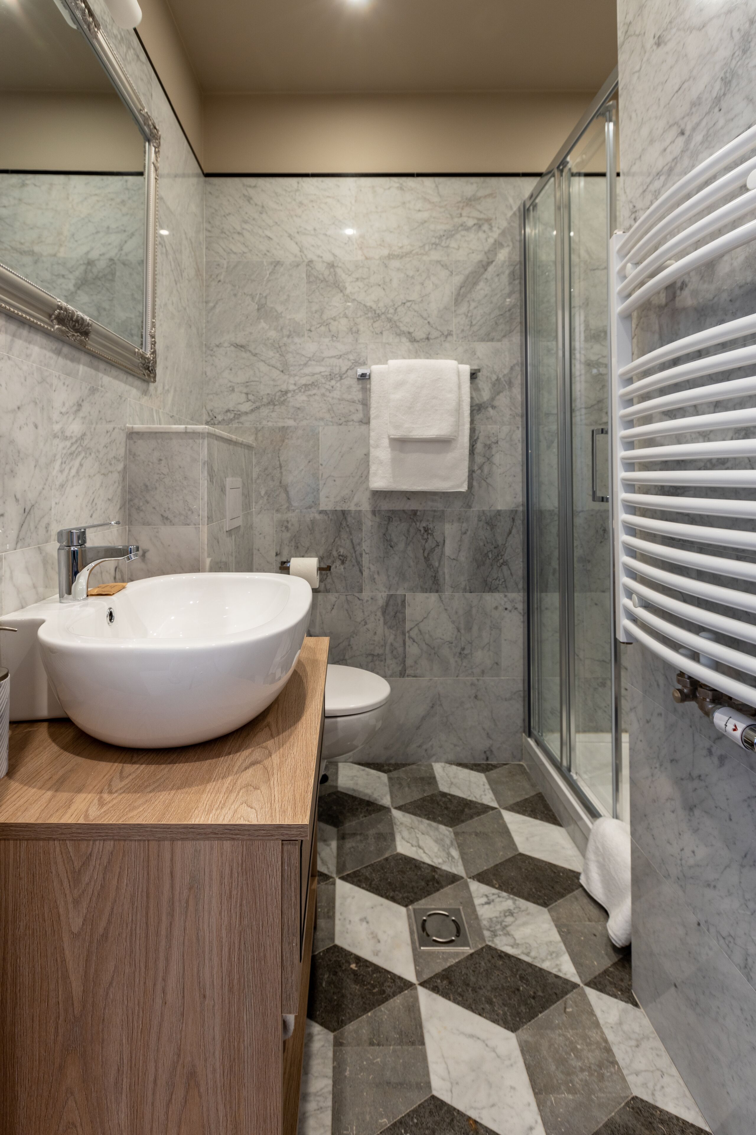 Un baño con un lavamanos grande de color blanco, una cabina de ducha de vidrio y suelo de baldosas de mármol.