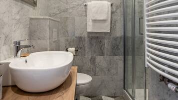 Un baño con un lavamanos grande de color blanco, una cabina de ducha de vidrio y suelo de baldosas de mármol.