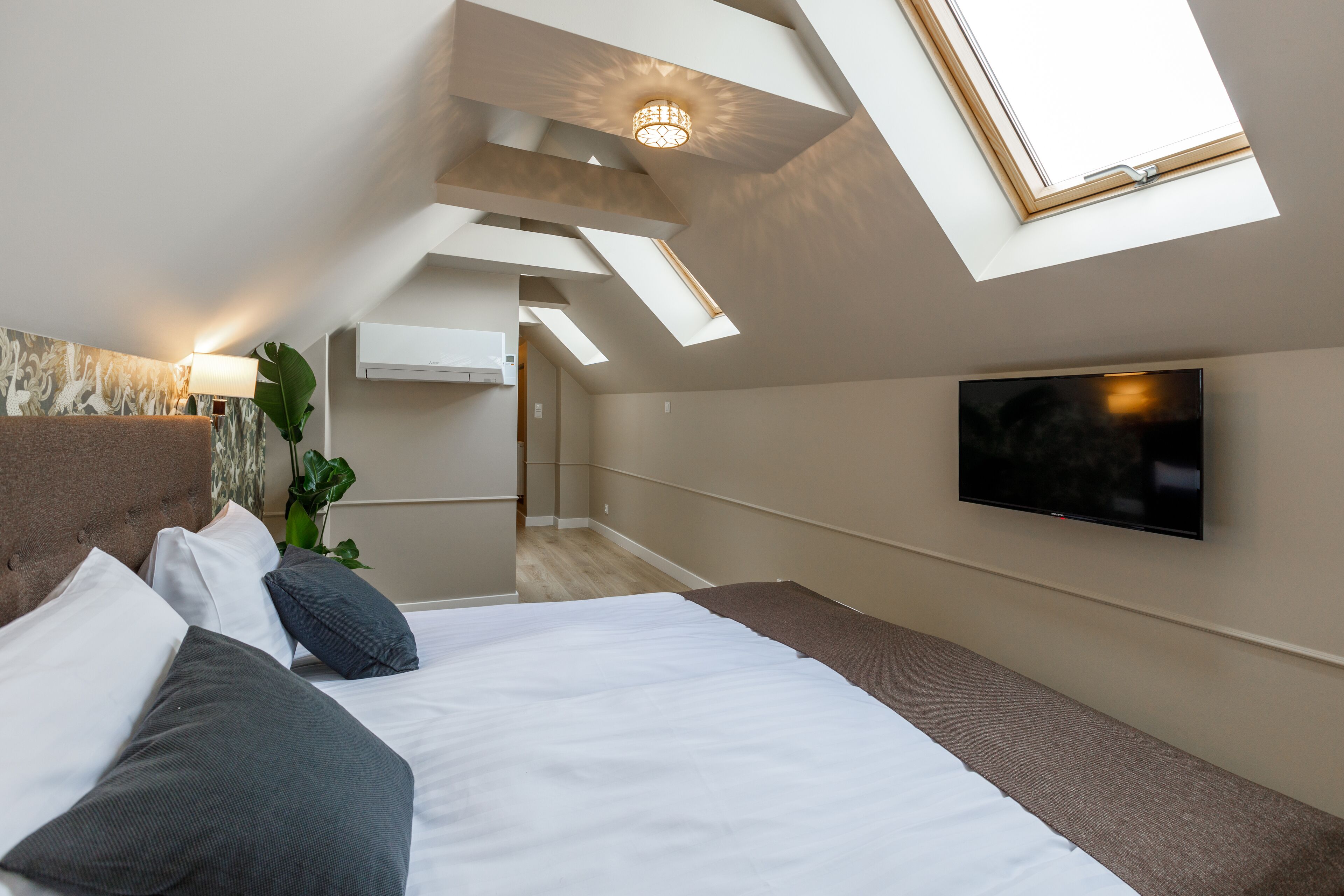 A modern bedroom with a skylight, a flat-screen TV, and a bed with multiple pillows.