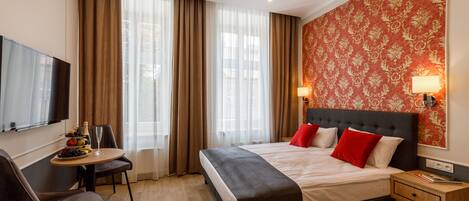 A hotel room with a large bed, a desk with a chair, a TV, and a wall-mounted lamp.