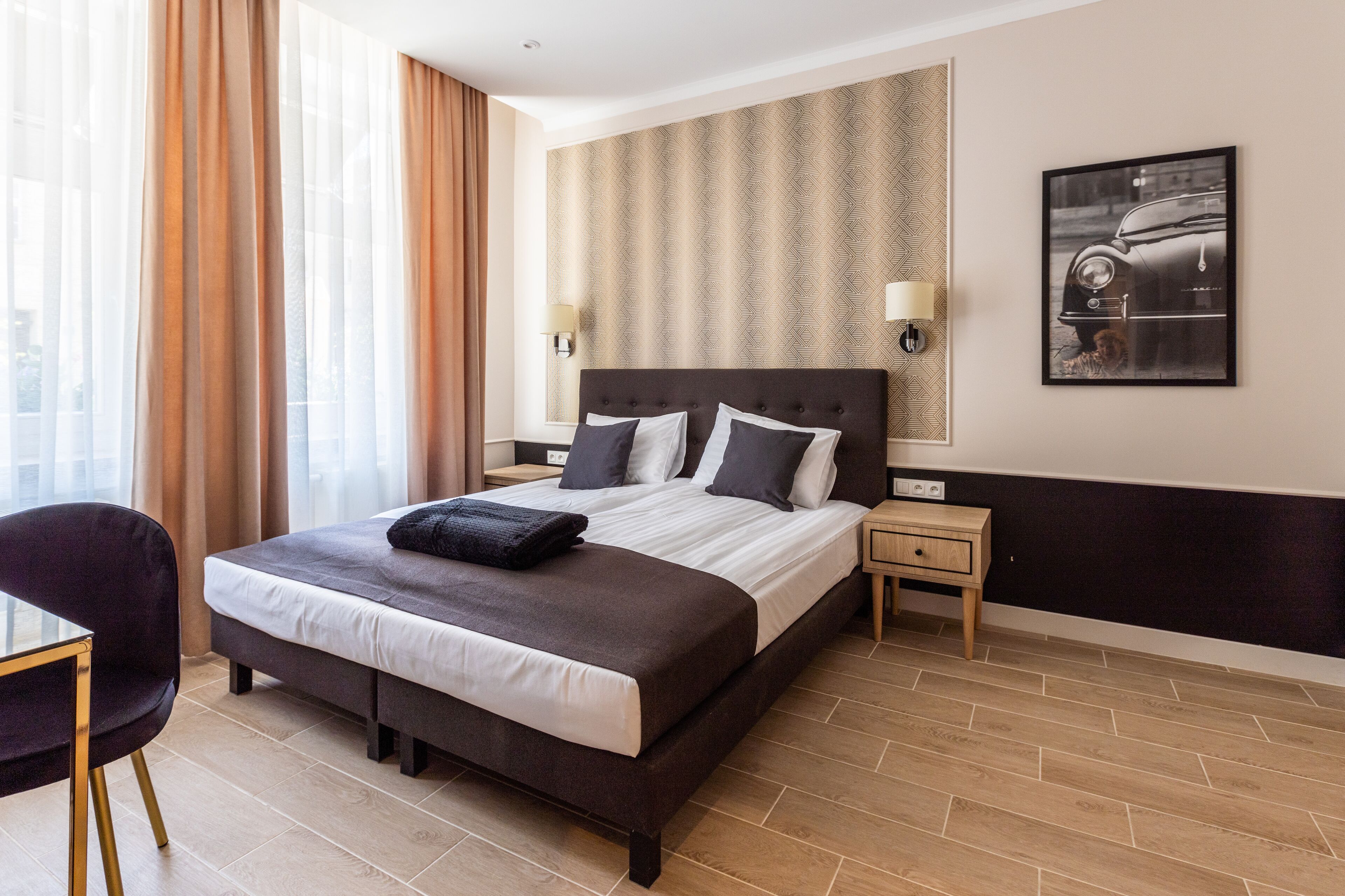 A hotel room with a large bed, two bedside tables, a chair, and a wall-mounted picture.