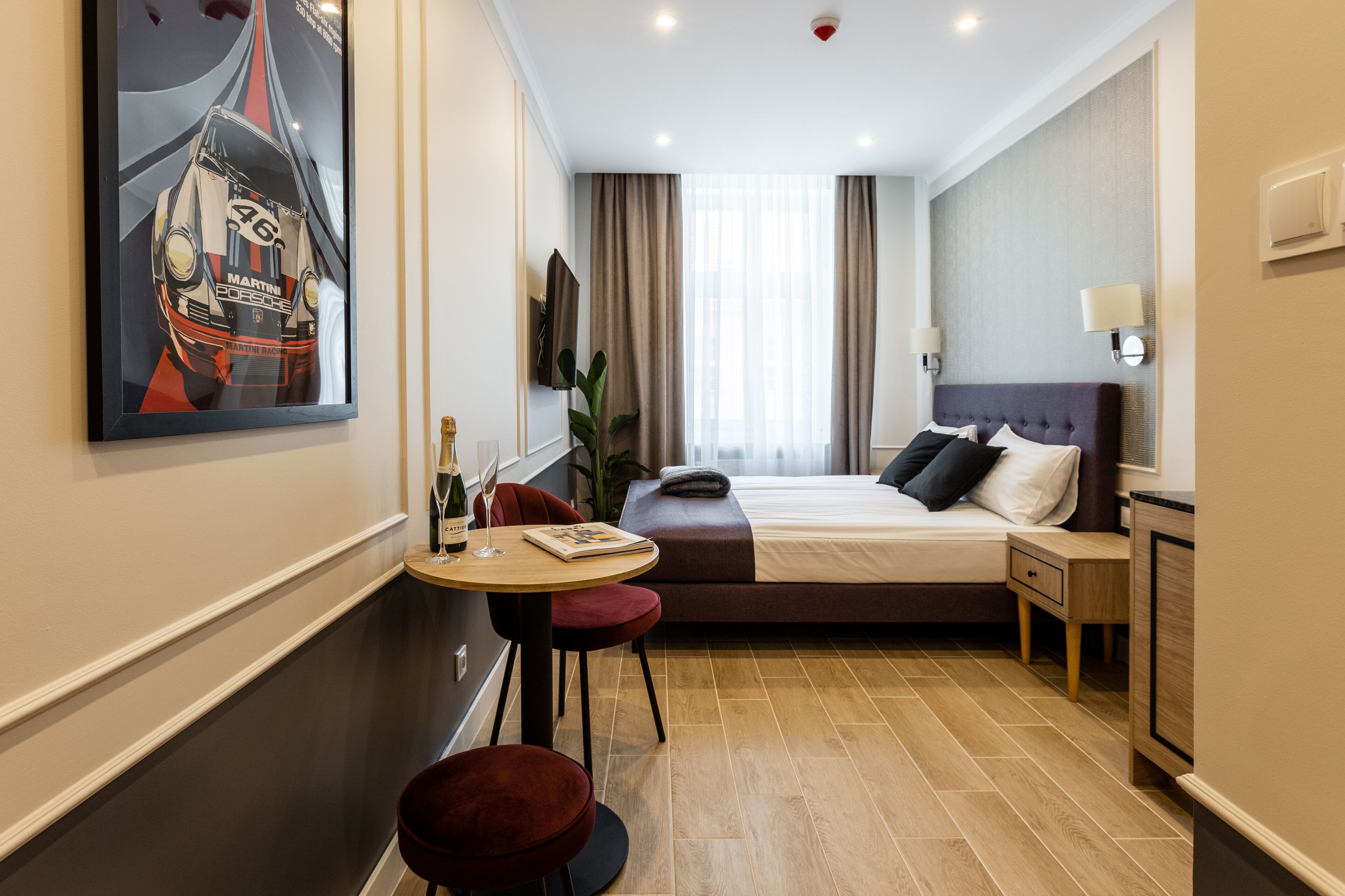 A modern hotel room with a bed, bedside table, lamp, and a large painting of a race car.