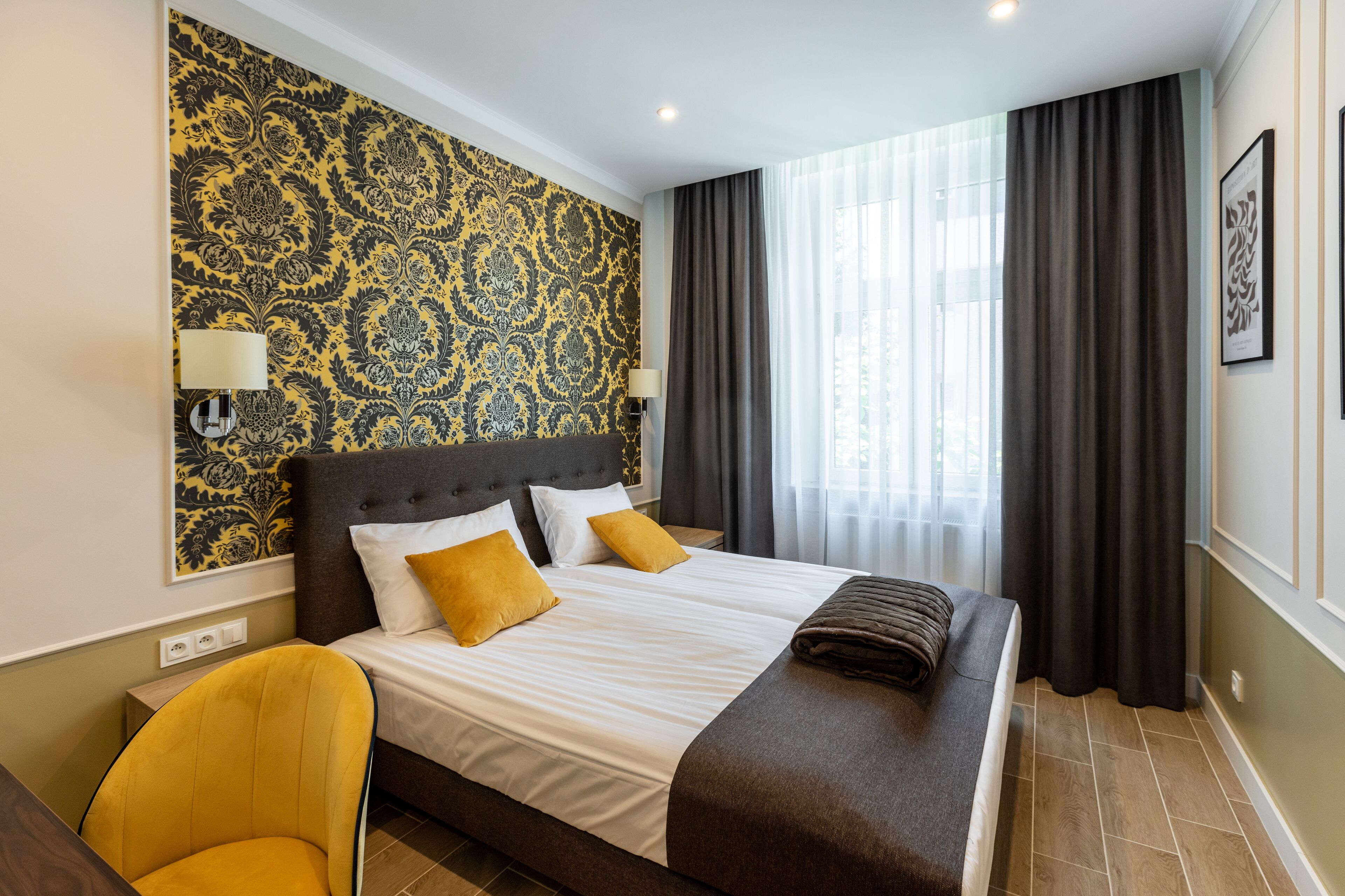 A hotel room with a large bed, two bedside lamps, a headboard, a window with curtains, and a chair.