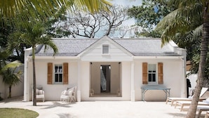 A white house with a tiled roof, a front porch with chairs, a pool, and palm trees.