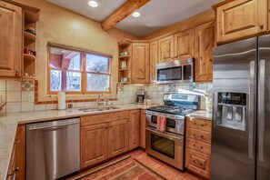 Una cocina con armarios de madera, electrodomésticos de acero inoxidable, una ventana y salpicadero de azulejos.