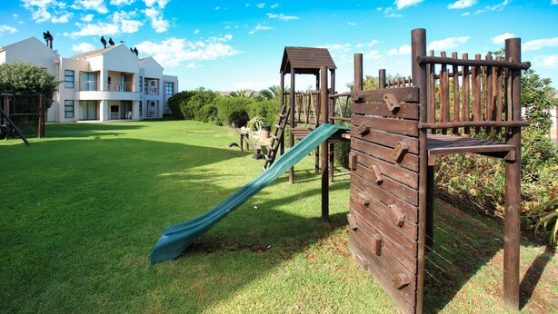 A playground with a slide and climbing structures, set against a backdrop of a residential building and a clear sky. - Ellefsen Golf Suite 115, Langebaan 4-Sleeper (Langebaan)