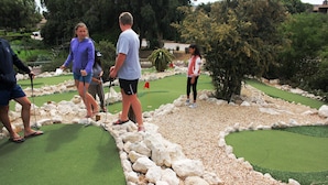 En minigolfbane med grøn putting-overflade, hvide sten og et rødt flag.