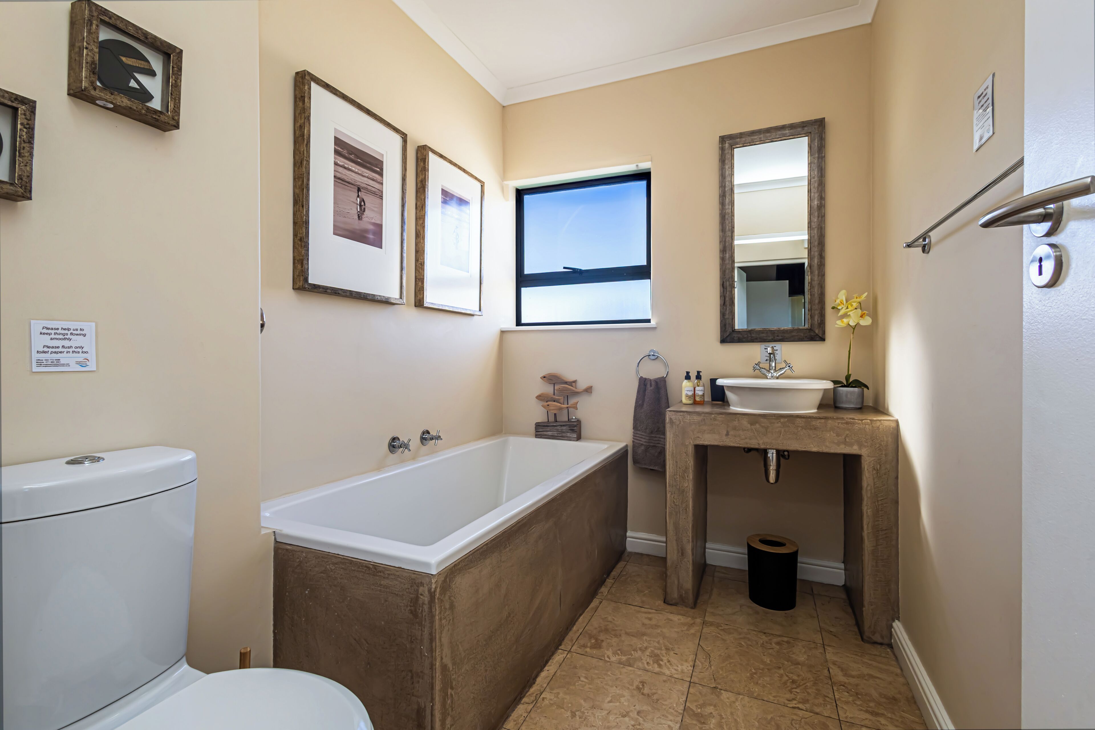 Une salle de bain avec une baignoire, des toilettes, un lavabo et des tableaux encadrés au mur.