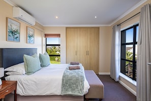 Une chambre à coucher avec un grand lit, une table de chevet, une fenêtre avec des rideaux et une vue sur la verdure.
