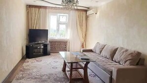 Un salon avec un canapé, une table basse en verre, un téléviseur posé sur un meuble et un tapis à motifs.