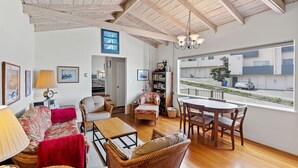 Un vaste salon doté d’un plafond en bois, un coin repas avec une table et des chaises, et une grande fenêtre donnant sur la rue.