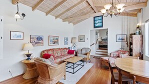 Un vaste salon doté d’un plafond en bois, d’un ensemble de canapés, d’une table à manger et d’un escalier menant à un autre niveau.