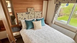 Une chambre à coucher avec un lit, une tête de lit en bois, une fenêtre avec des rideaux et une porte donnant sur une autre pièce.