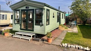 Une petite maison mobile d’un seul étage, de couleur verte, portant le numéro 13, avec une véranda à l’avant et un petit jardin.