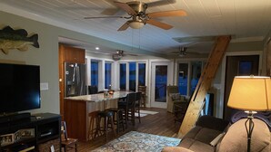 Ein Wohnzimmer mit Fernseher, Deckenventilator aus Holz, Sofa, Couchtisch und einem gemusterten Teppich.