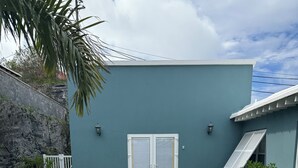 Ein Weg führt zu einem Haus mit blauer Fassade, einer weißen Tür und je einem Blumentopf auf beiden Seiten.