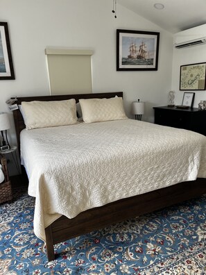 A neatly made bed with a quilted white bedspread, a dark wooden headboard, and a blue patterned carpet.