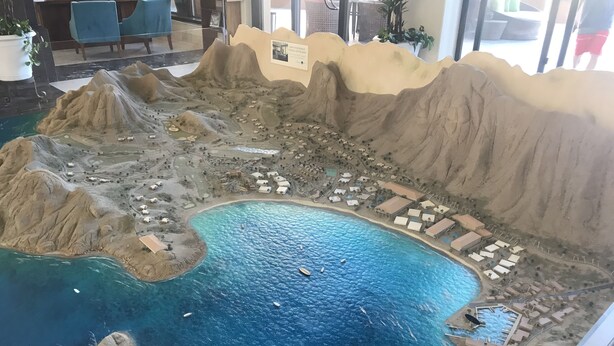 Un model d'un complex turístic costaner amb una piscina central, diversos edificis i un litoral rocos.