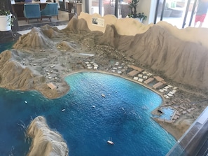 Une maquette d’un complexe hôtelier en bord de mer, doté d’une piscine centrale, de plusieurs bâtiments et d’une côte rocheuse.