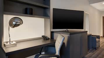A modern hotel room with a desk, chair, TV, and built-in shelving.