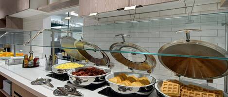 A buffet with various food items including waffles, eggs, and bacon.