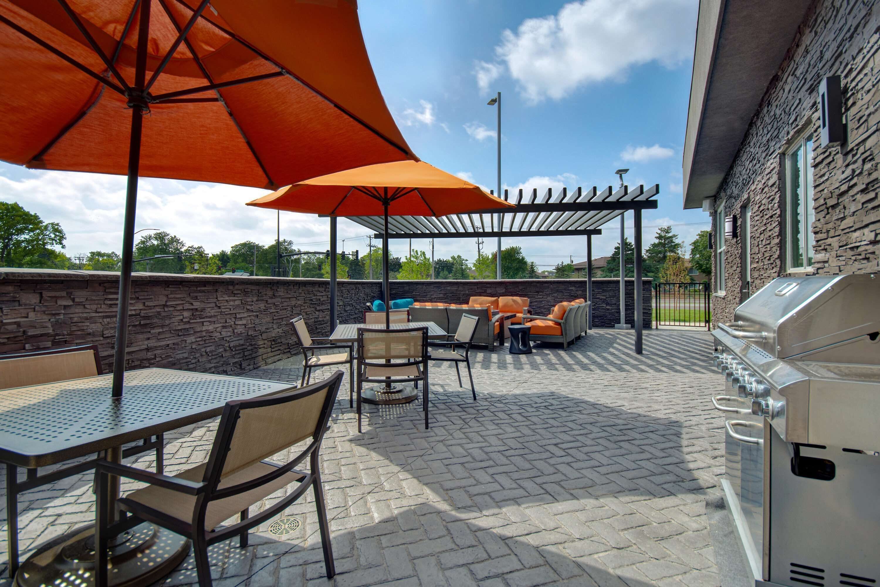 Een terras buiten met een barbecue, zitplaatsen en parasols.