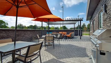 Een terras buiten met een barbecue, zitplaatsen en parasols.