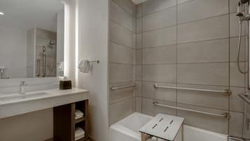 A modern bathroom with a large mirror, a sink, a shower with grab bars, and a bathtub.