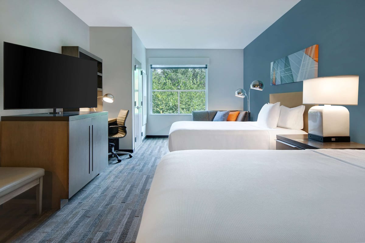 Une chambre d’hôtel avec deux lits, une télévision, un bureau et une fenêtre donnant sur des arbres.