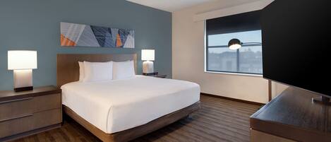 A hotel room with a large bed, two bedside tables with lamps, a flat-screen TV, and a window with a view of a cityscape.
