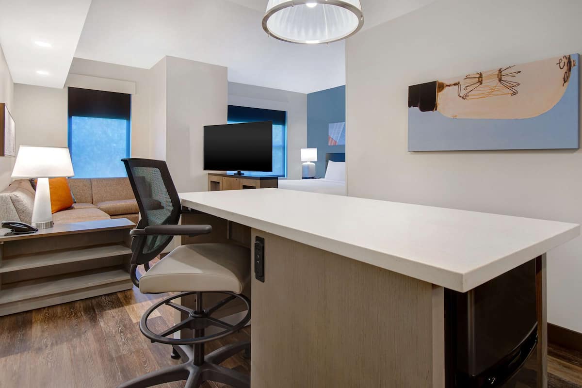 Une chambre d’hôtel moderne, dotée d’un grand bureau, d’une télévision, d’un canapé et d’un tableau au mur.