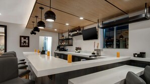 A modern bar area with a long counter, bar stools, and a TV mounted on the wall. - Hyatt House Mall Of America Msp Airport (Bloomington)