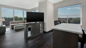 A modern living room with a large TV, a sofa, and a dining area with a view of the city. - Hyatt House Mall Of America Msp Airport (Bloomington)