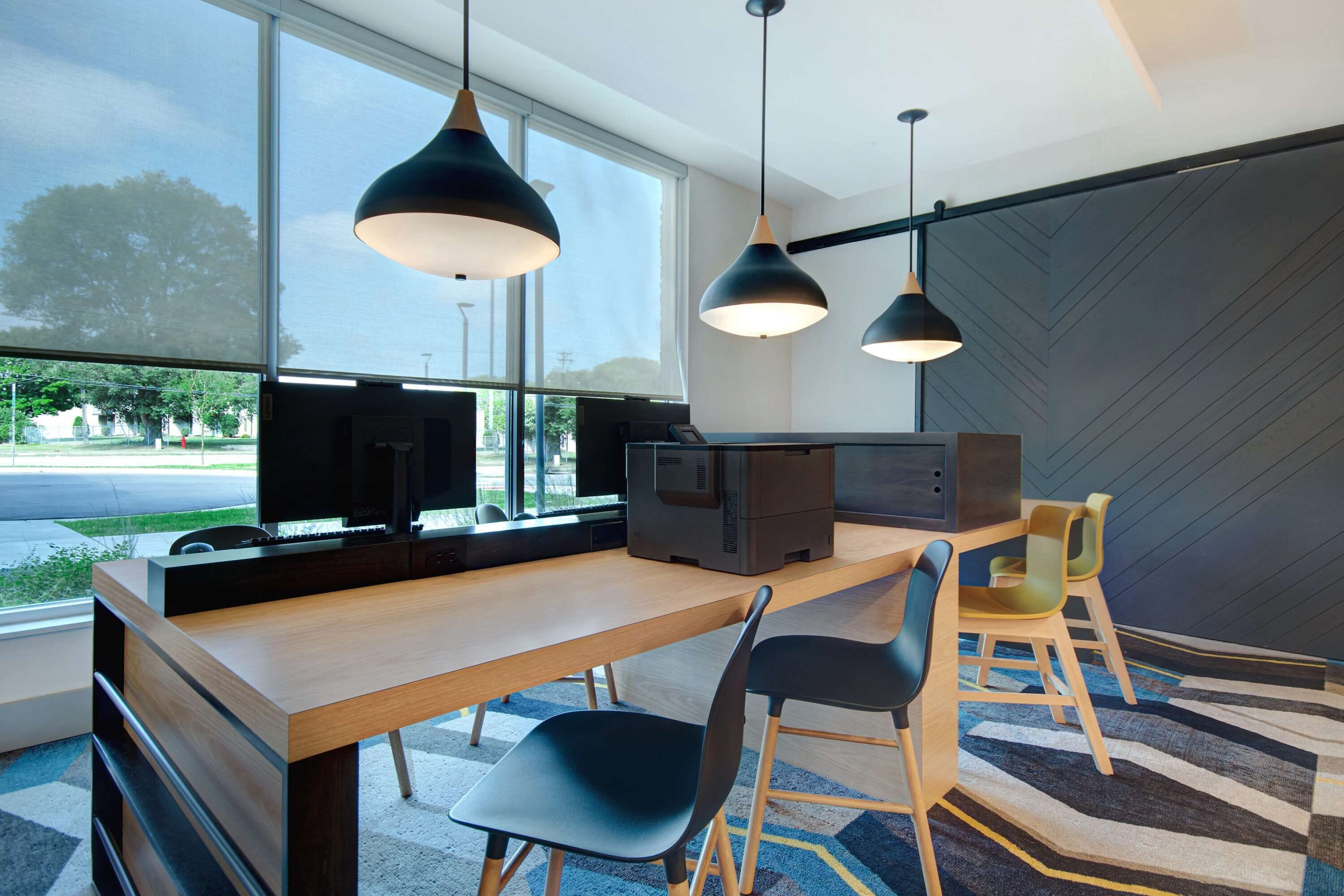 Un espacio de oficina moderno con una larga mesa de madera, sillas negras e iluminación colgante.