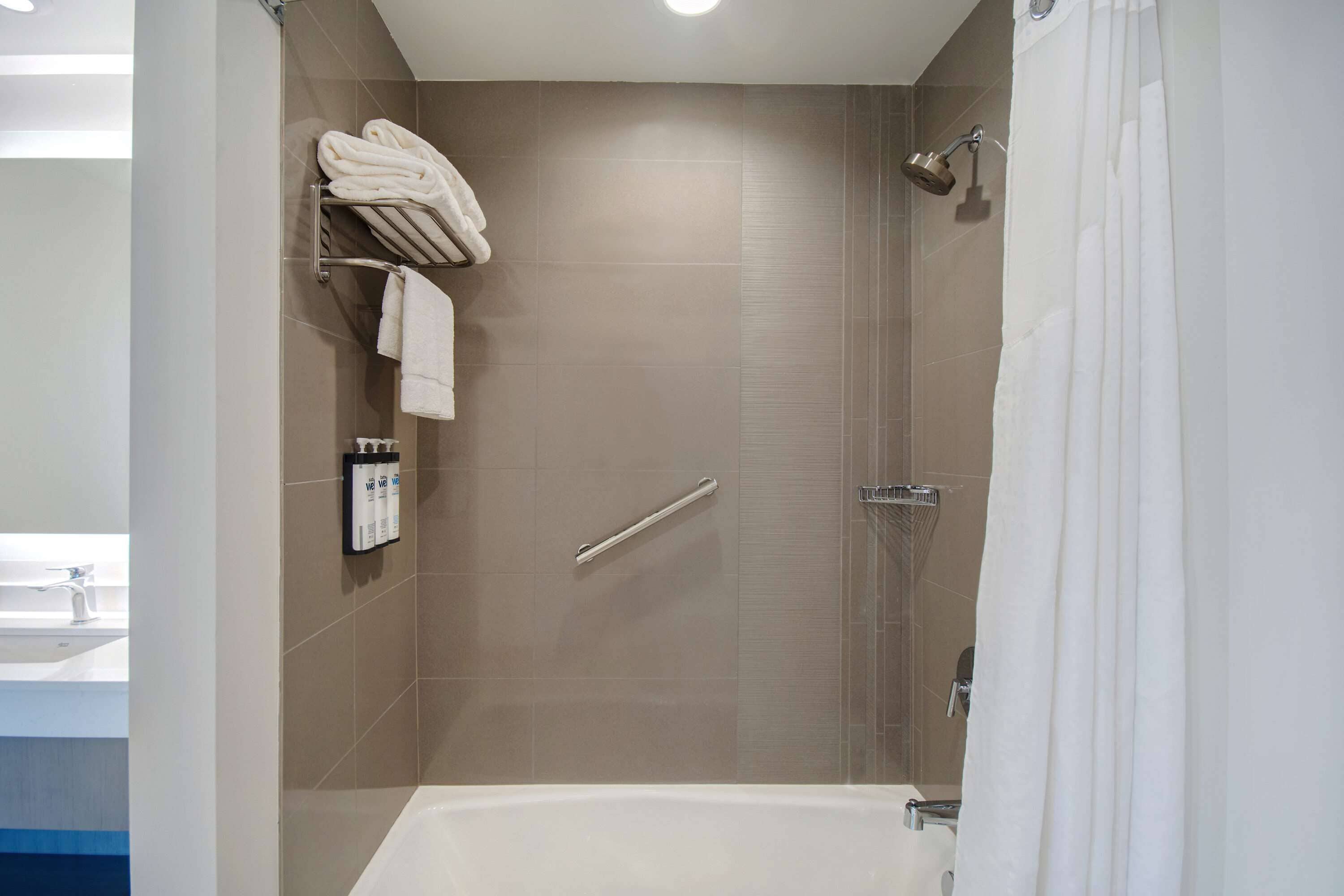 Un baño moderno con ducha a ras de suelo, bañera y toallero con toallas dobladas.