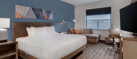 Habitación de hotel con una cama grande, un escritorio, una silla, un televisor y una ventana.