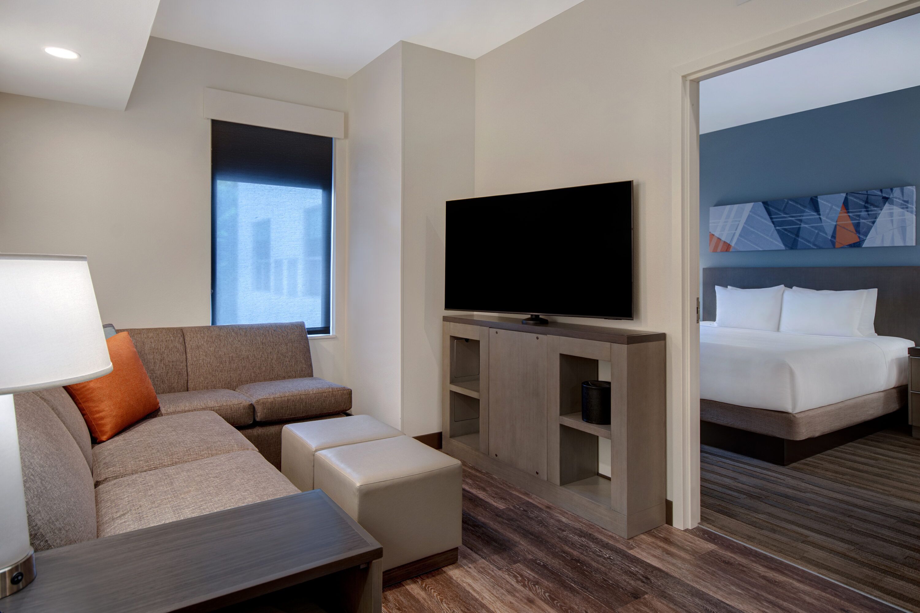 A modern hotel room with a sofa, TV, and a bed.