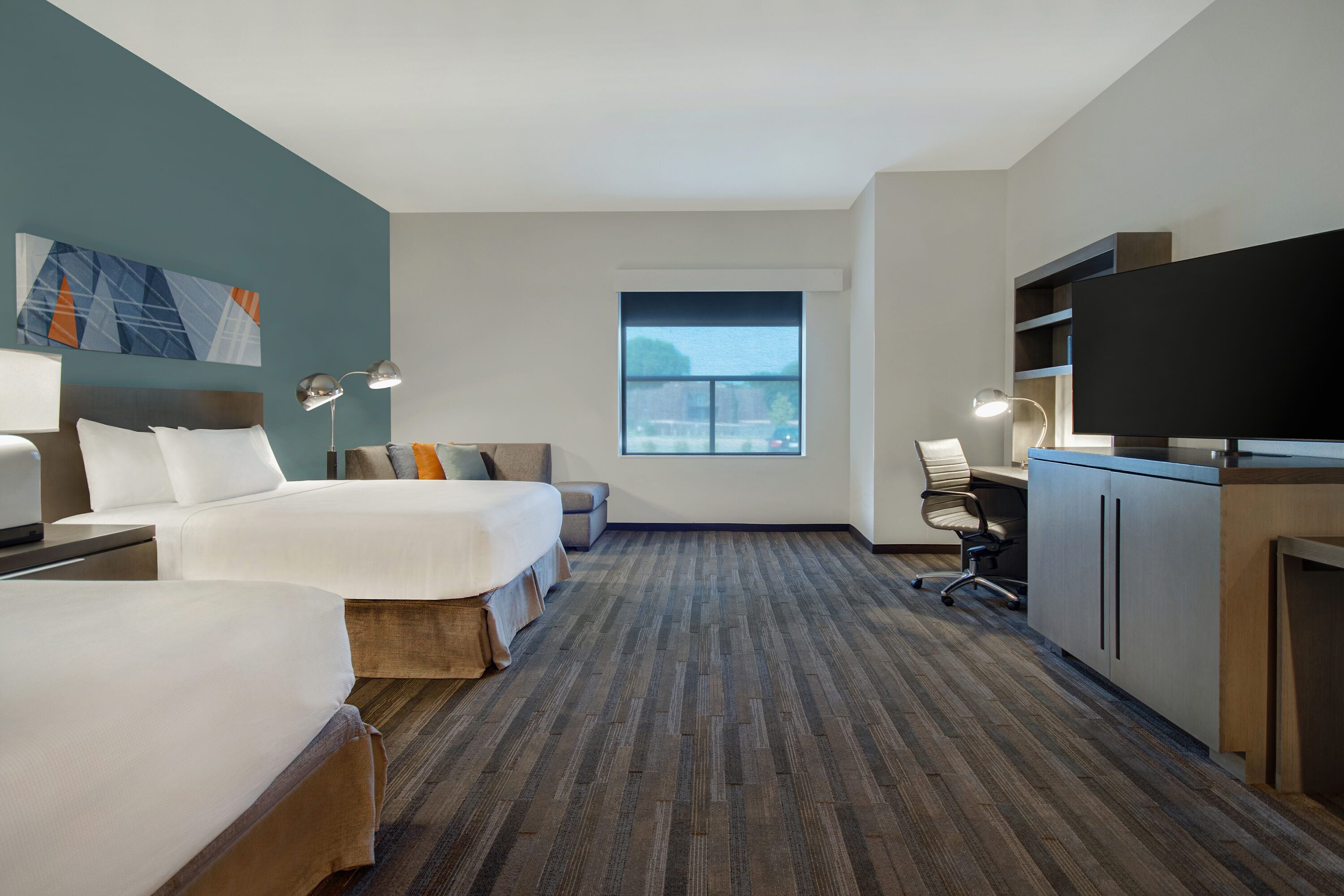 A hotel room with two beds, a desk, a television, and a window with a view.