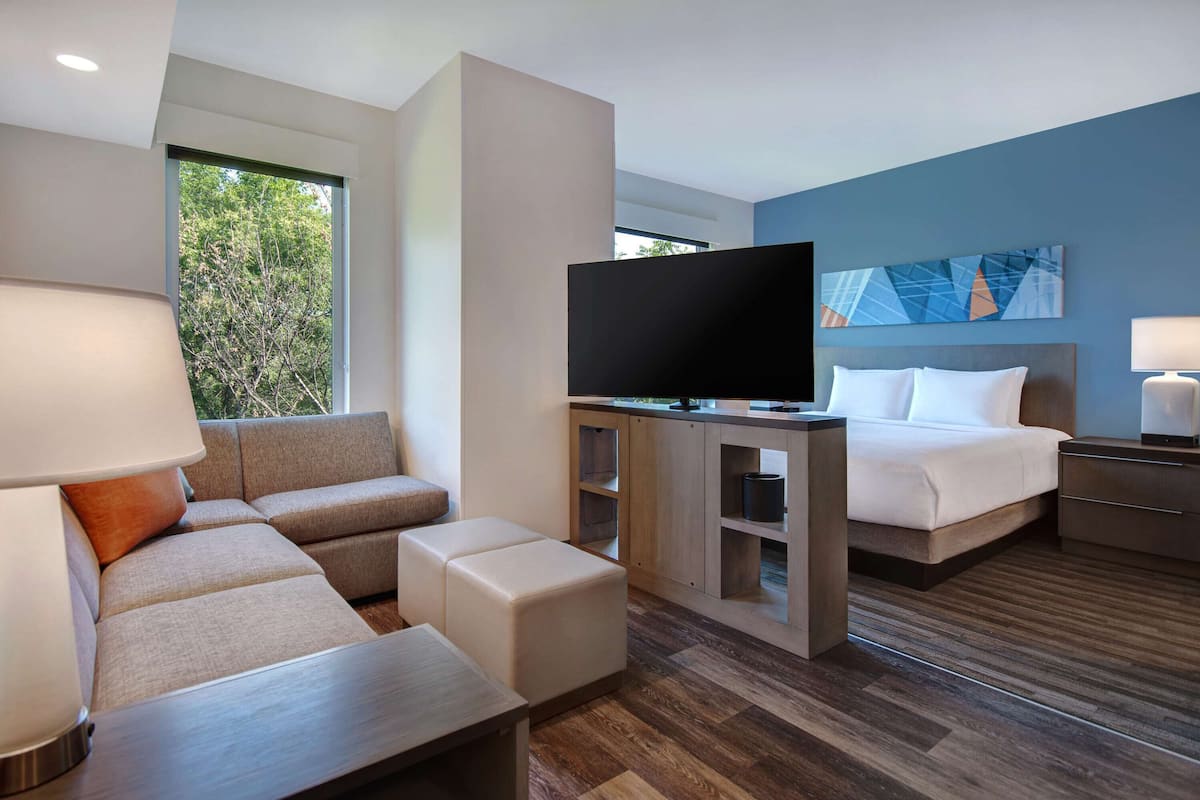 Une chambre d’hôtel moderne avec un canapé, un téléviseur posé sur un meuble en bois, un lit et une table de chevet.