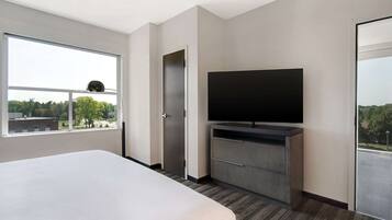 A modern hotel room with a large bed, a flat-screen TV, a wardrobe, and a window offering a city view.