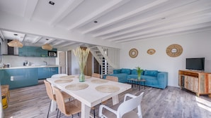 Una cocina moderna con armarios color turquesa, una mesa de comedor blanca con individuales tejidos, y un sofá azul en la sala.