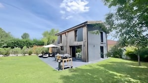 Una casa moderna de dos pisos con un amplio jardín delantero, un patio y un automóvil estacionado afuera.