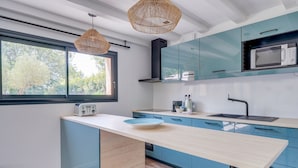 Una cocina moderna con armarios color turquesa, una isla de madera, un microondas y un ventanal con vistas a árboles.