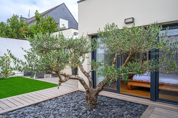 Uma casa moderna com um jardim bem cuidado, um deck de madeira e um quarto com paredes de vidro.