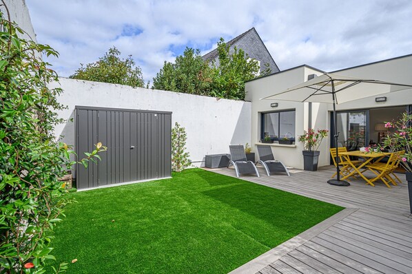 A modern outdoor patio with a neatly trimmed lawn, a grey metal gate, and a seating area with yellow chairs and a table. - LA P'TITE VANNETAISE - Petite maison au bord de l'eau à Conleau avec vélos ! (Vannes)